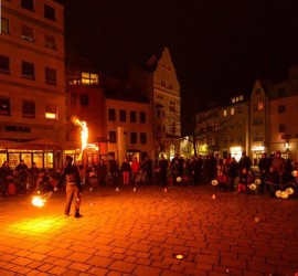 Eine Person macht Feuershow, rundherum viele Menschen mit Lampions, im Hintergrund Häuser