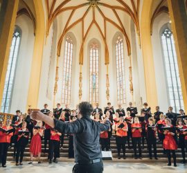 Blick von unten auf singenden Chor während eines Konzertes, Chorlieter Fabian Pasewald im Vordergrund und das Gewölbe über dem Altarraum im Hintergrund
