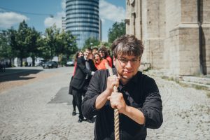 Fabian Pasewald zieht vor der Stadtkirche an einem Seil, im Hintergrund unscharf der Chor, am anderen Ende des Seils ziehend